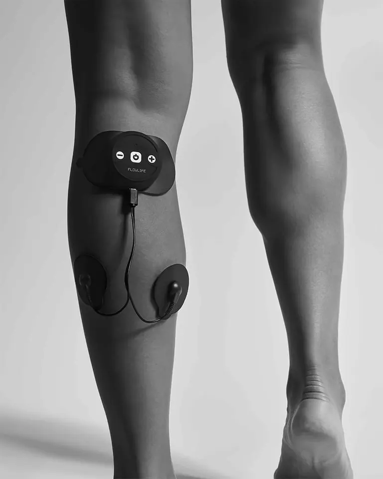 Black Flowtens Connect TENS device and electrode pads applied to a calf muscle for targeted nerve stimulation.