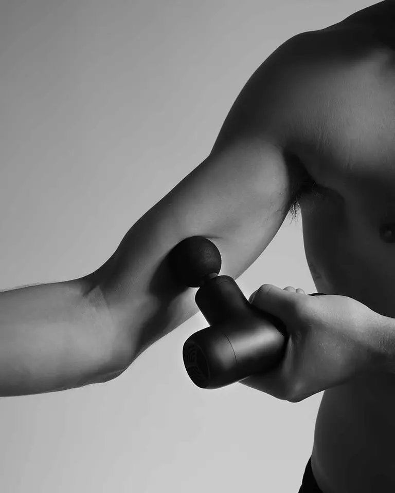 A person using the black Flowgun Air on their upper arm for targeted percussive therapy and muscle recovery.