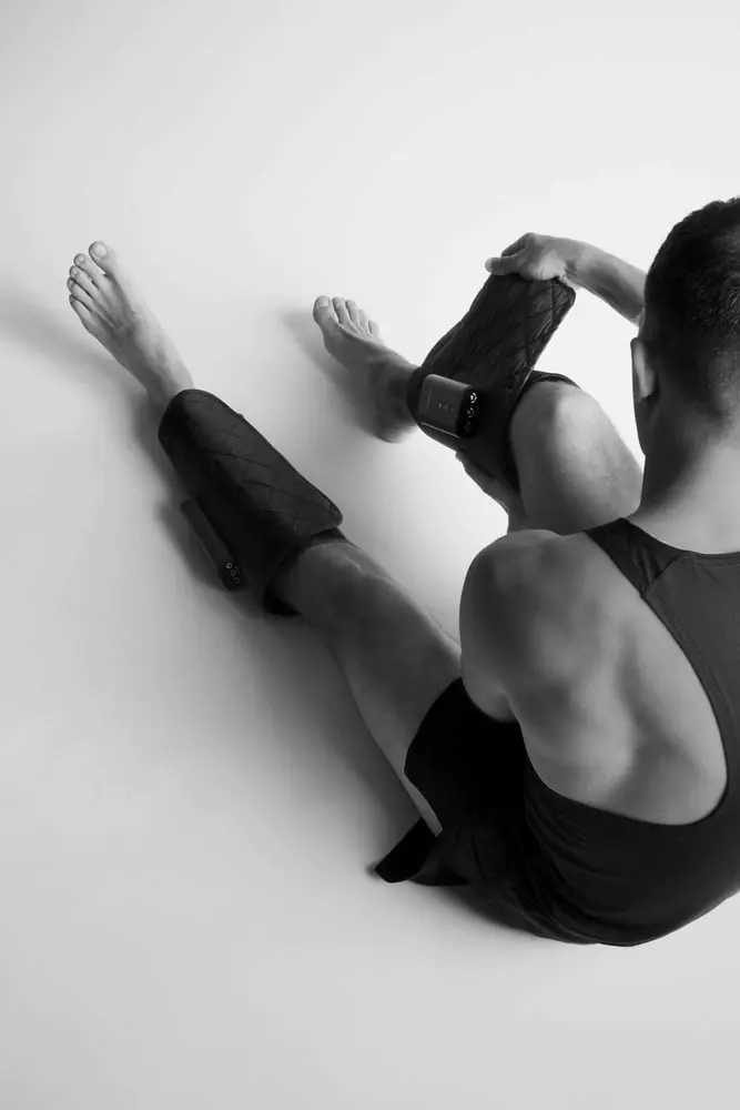 A man wearing black Flowpression Calf DUO cordless air compression sleeves for calf muscle recovery and circulation.
