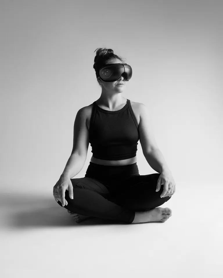 Woman wearing Flowpression Goggles while sitting cross-legged in a studio for eye compression therapy.