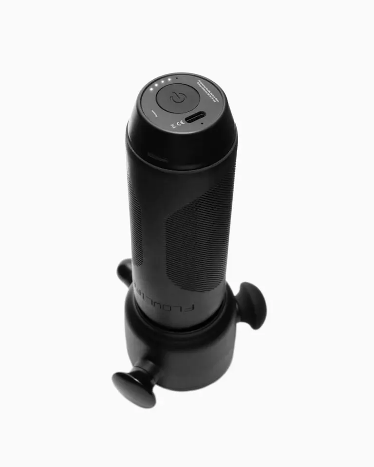 A top angled view of the black Flowsonic Pro vibration therapy device, showing power button, LED indicators, and USB-C port.