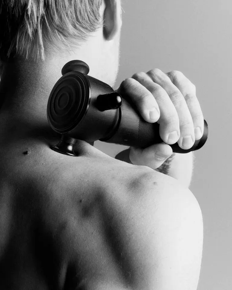 Black Flowsonic Pro vibration therapy tool applied to the shoulder for gentle, surface-level muscle recovery.