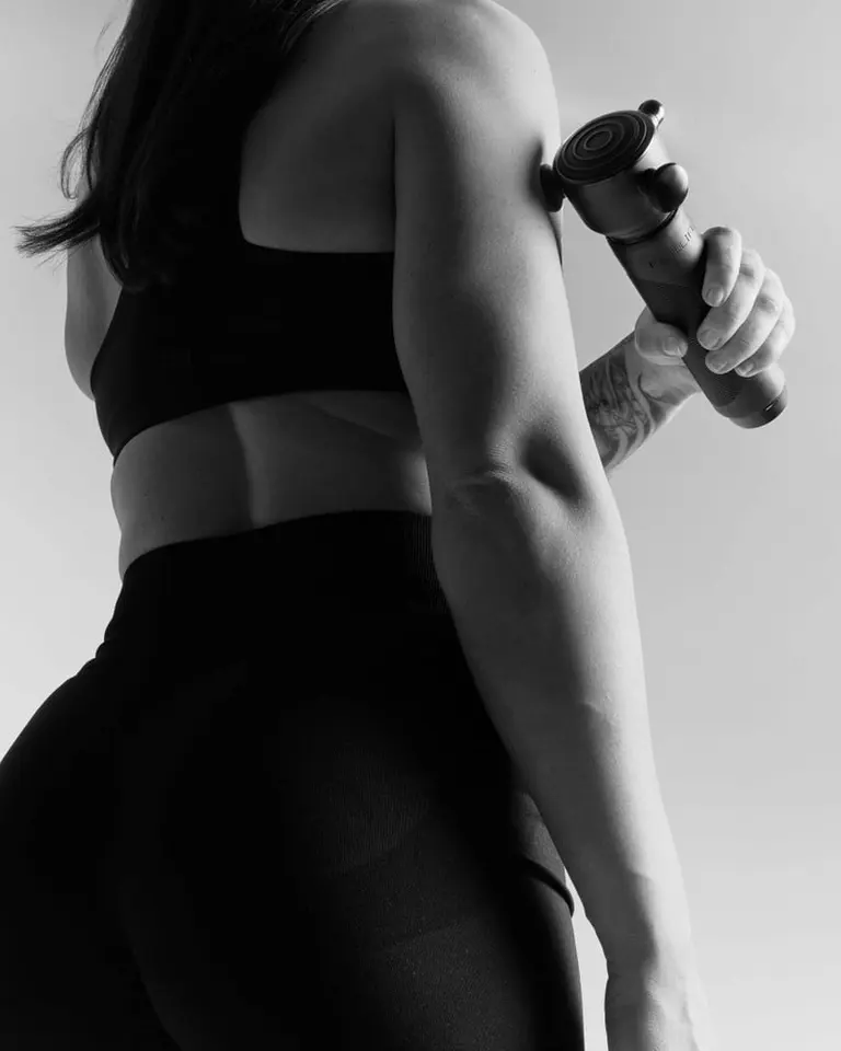 Flowsonic Pro+ vibration therapy device applied to a shoulder for targeted relief in a black-and-white studio image.