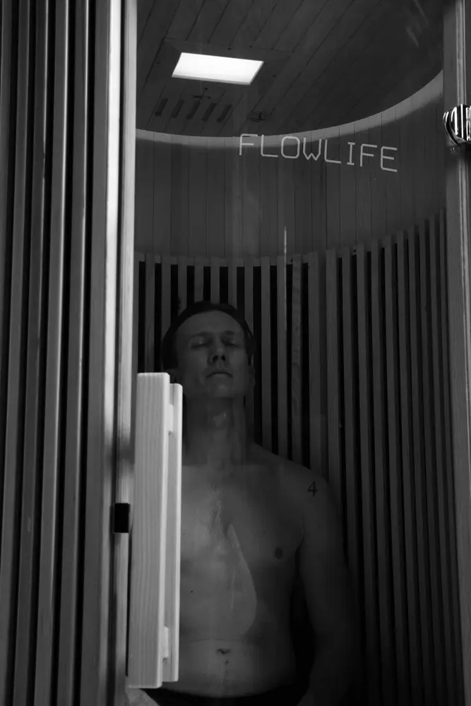 A man relaxes inside the Flowsauna Elite Solo, a far-infrared sauna cabin with a hemlock wood interior.