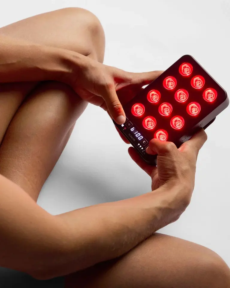 Handheld Flowlight Panel Go 60 Two Waves with glowing red LEDs held against a thigh for targeted muscle recovery.