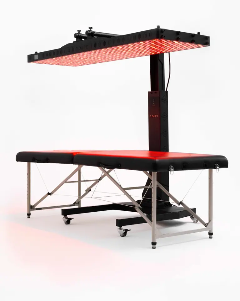 Flowlight Auto Static Stand in black, positioning an active red light therapy panel over a professional treatment table.