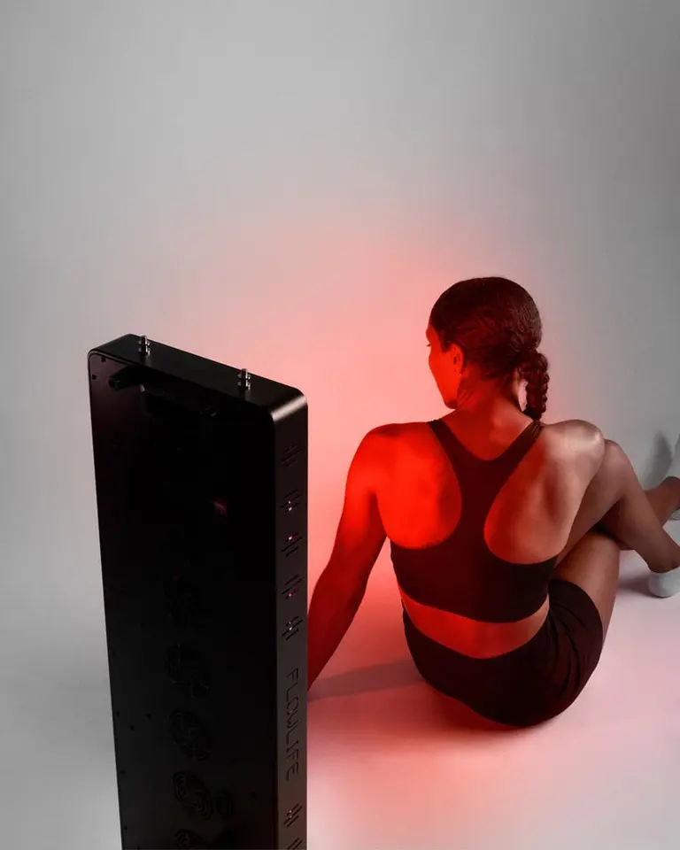 A woman seated in front of the Flowlight Panel 1500 Seven Waves for targeted red light therapy on her back.