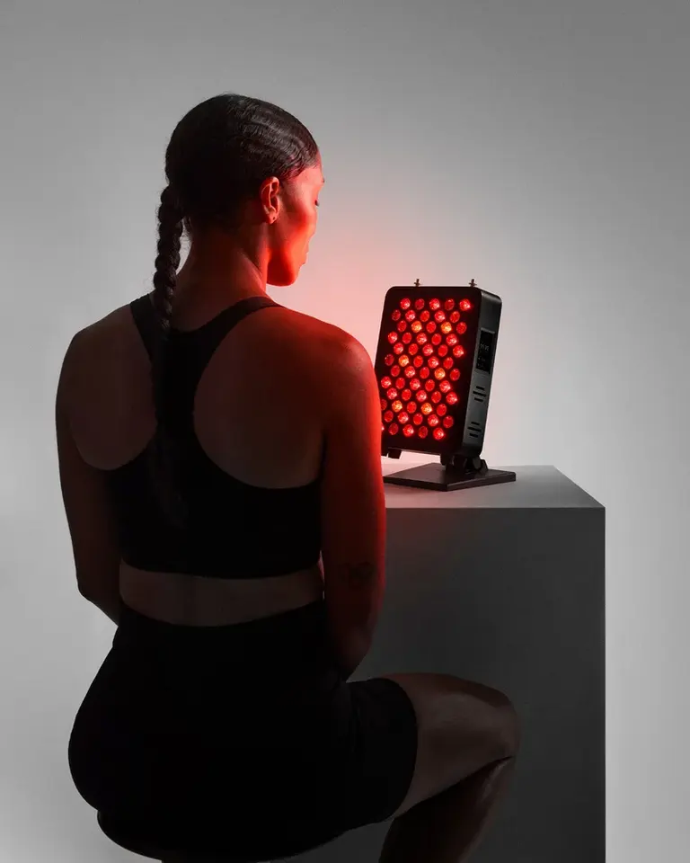 User seated in front of a Flowlight 300 Seven Waves red light therapy panel with an illuminated red LED array.