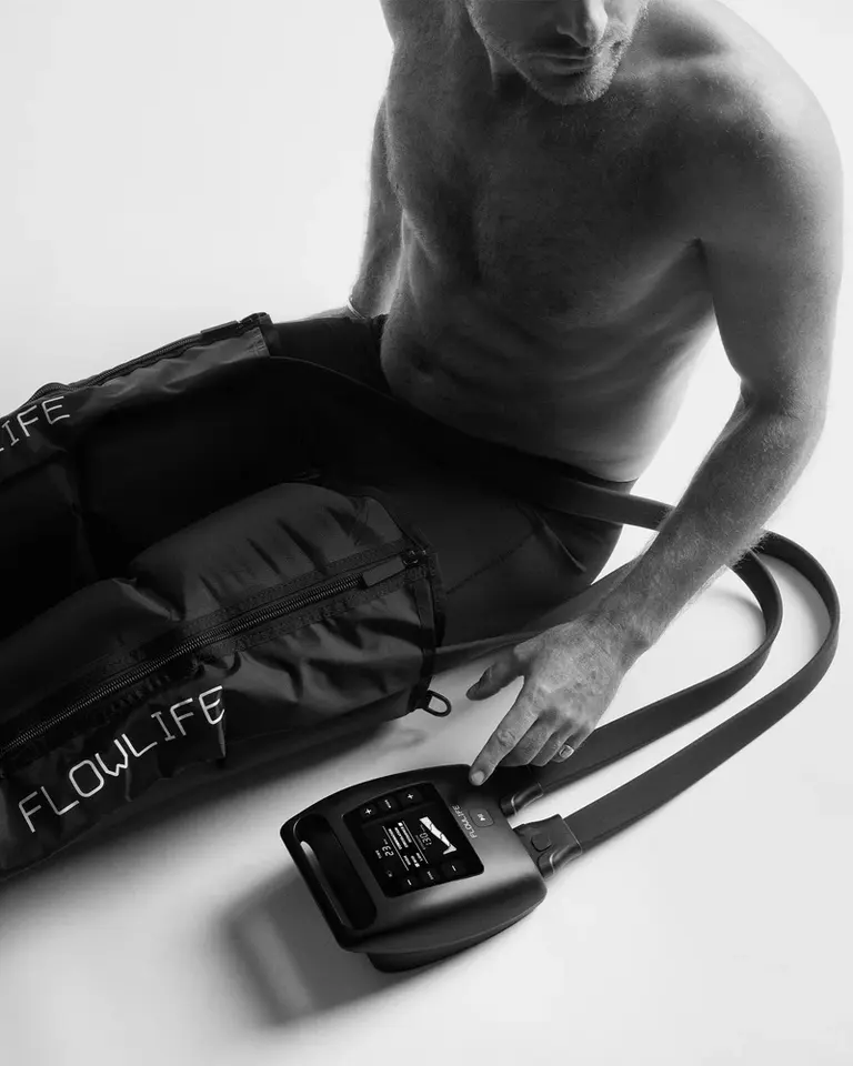 A man operates the digital control unit for the black Flowpression Boots Pro+ S to manage leg compression therapy.