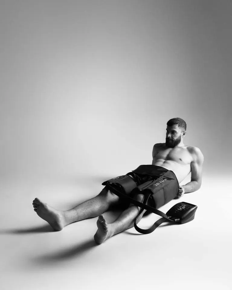 A man using the black Flowpression Hip Pro attachment and Pro+ control unit for targeted pneumatic compression therapy.