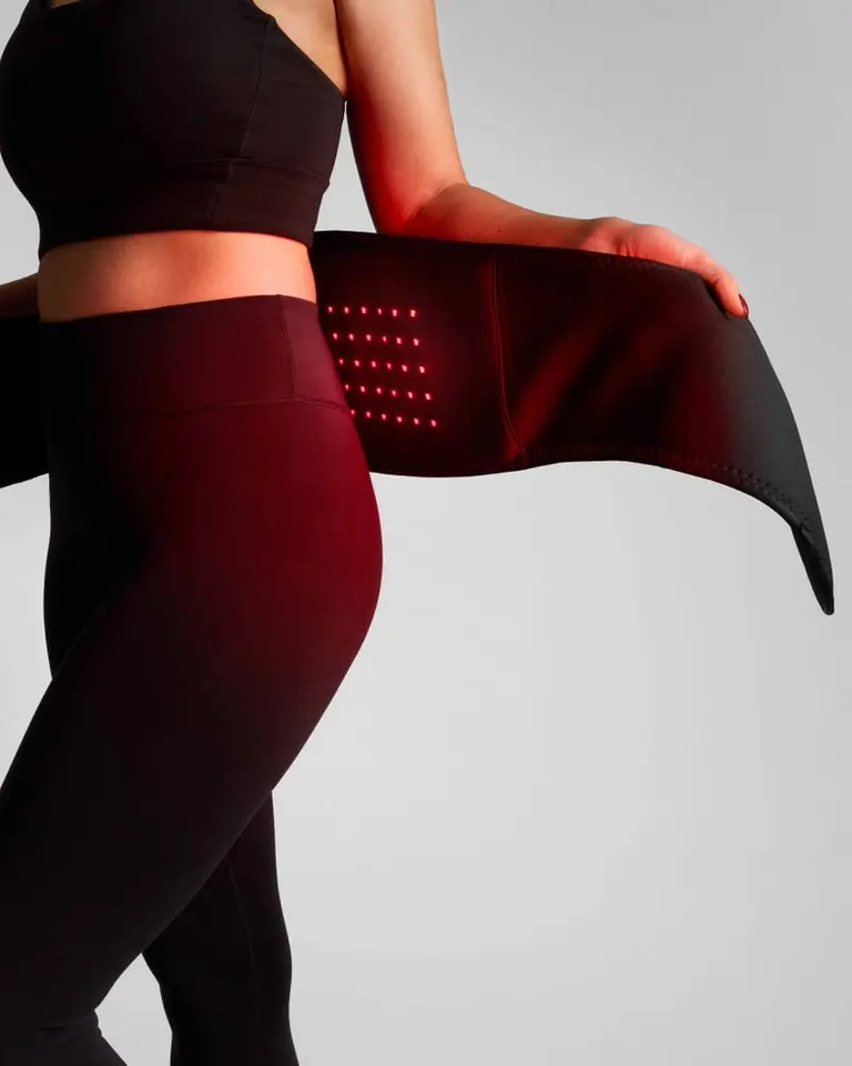 A person wearing the black Flowtherma Belt, showing the illuminated red light LEDs for targeted lower back recovery.
