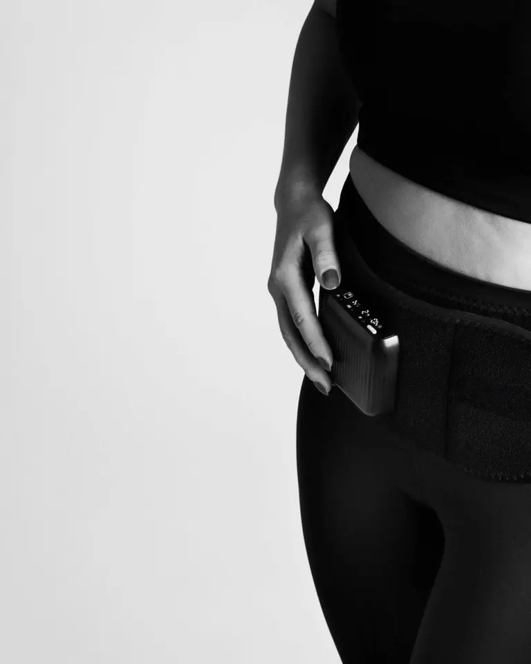 A close-up of the Flowtherma Belt worn for lumbar support, shown in black and white with a hand on the control unit.