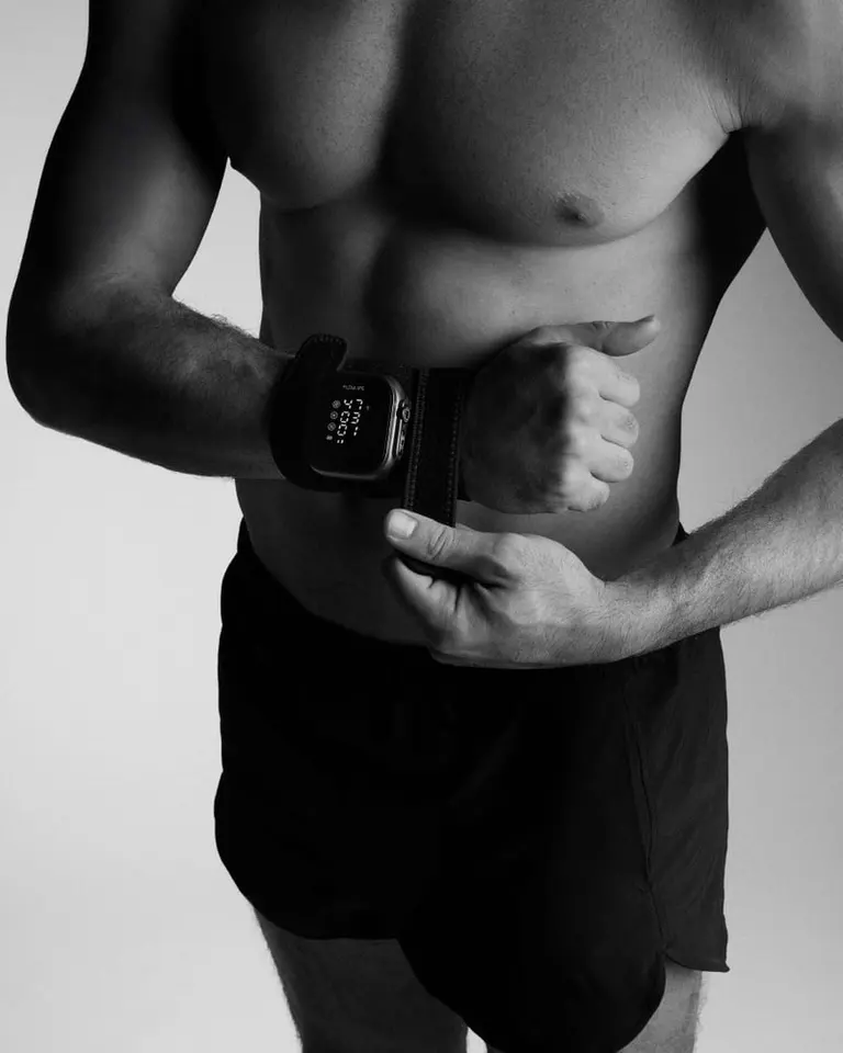 A man secures the Flowtherma Spot to his wrist with a Velcro strap for targeted heat, light, and vibration therapy.