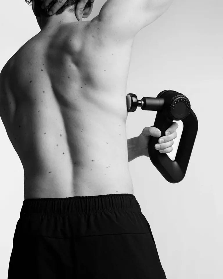 Flowgun Ultra used for back muscle recovery, highlighting its ergonomic triangular handle in a black and white studio.