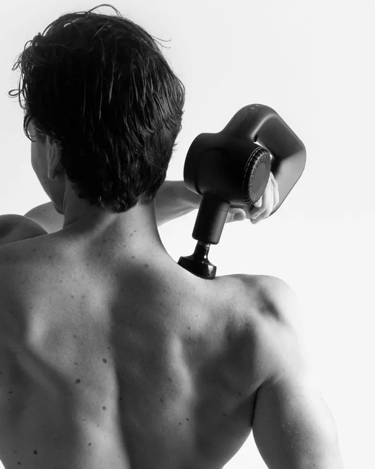 The black Flowgun Ultra used on a person's shoulder for muscle recovery in a black and white rear-view photo.