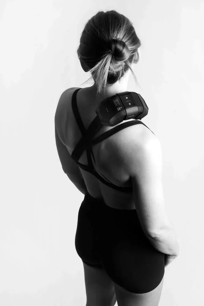 Back view of a woman wearing the black Flowcontrast Spot Go device strapped to her upper back for contrast therapy.