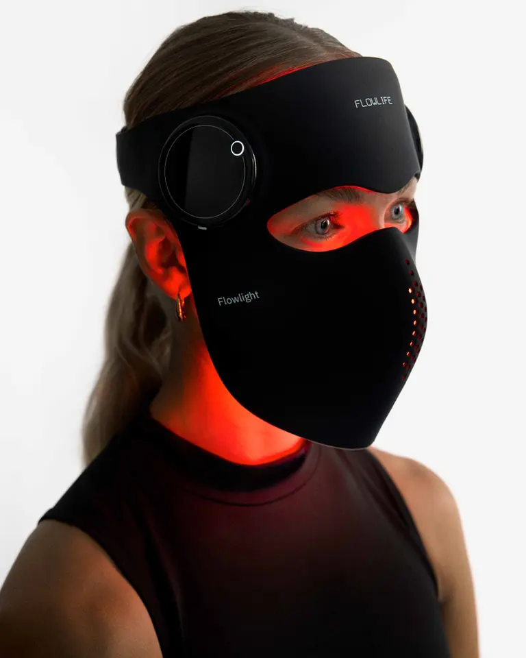 A woman wearing the black silicone Flowlight LED Mask Pro Two Waves with active red light therapy for recovery.