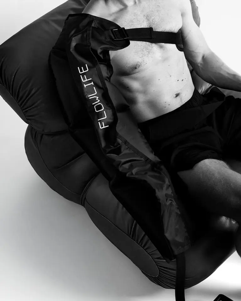 Black Pro+ Arm Attachment worn by a person reclined in a chair for sequential arm compression and recovery.