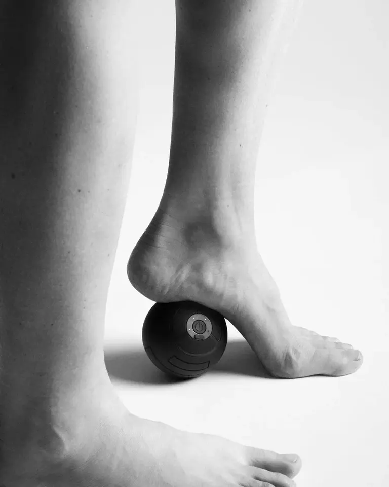 Black Flowroller Ball Go positioned under a foot for targeted vibration massage and trigger point release.